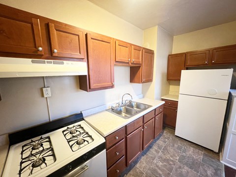 A kitchen with white appliances and brown cabinets.at North Pointe Commons Apts, Pittsburgh, PA